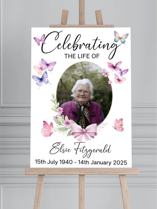 Personalised celebration of life memorial sign featuring a floral butterfly design with a photo of a loved one, custom name and dates, printed on white foam board and displayed on a wooden easel for a funeral or memorial service.