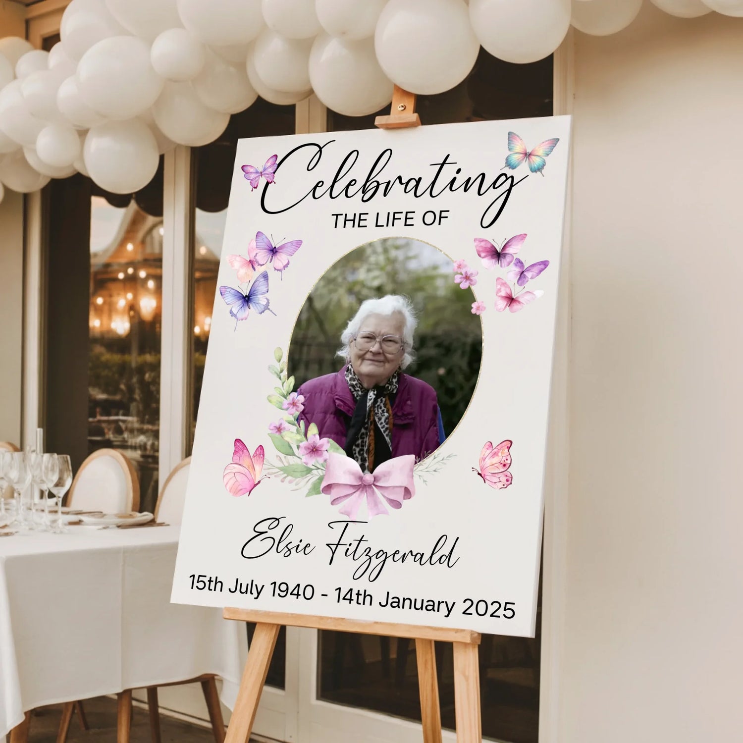 Personalised celebration of life memorial sign featuring a floral butterfly design with a photo of a loved one, custom name and dates, printed on white foam board and displayed on a wooden easel for a funeral or memorial service.